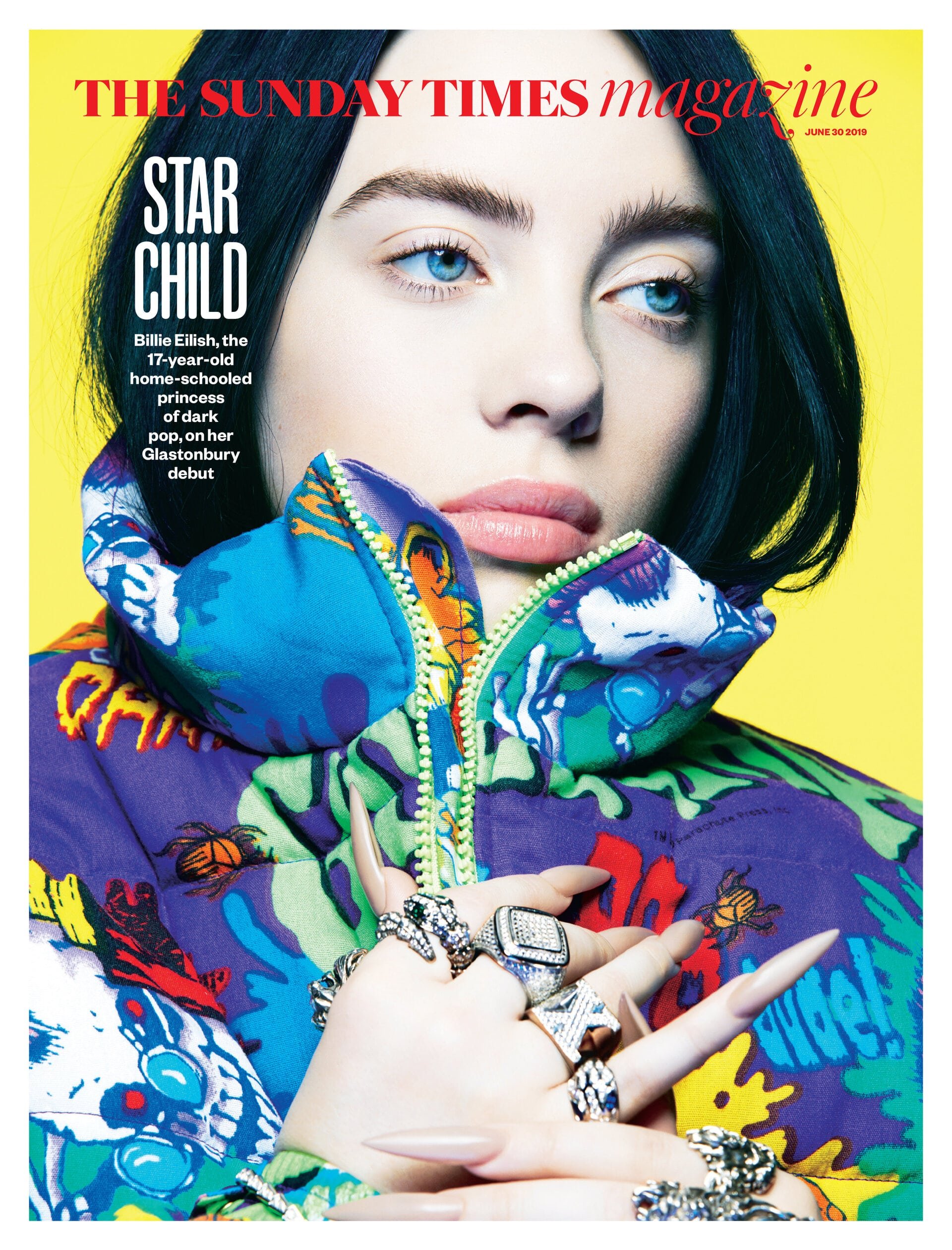 Magazine cover featuring a young adult female with pale skin, dark hair, and bright blue eyes, wearing an ornate puffy coat and many rings.