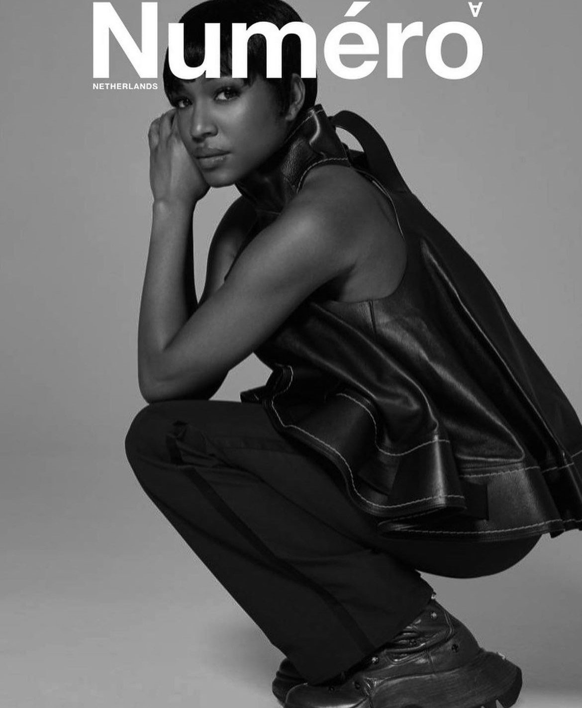Magazine cover featuring a Black woman in a crouched pose, wearing a leather top and black pants, in a black-and-white studio shot.
