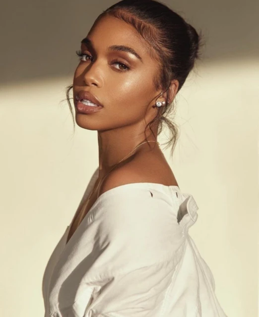 Portrait of a woman with brown hair and fair skin wearing an off-the-shoulder white shirt in front of a gradient cream background.