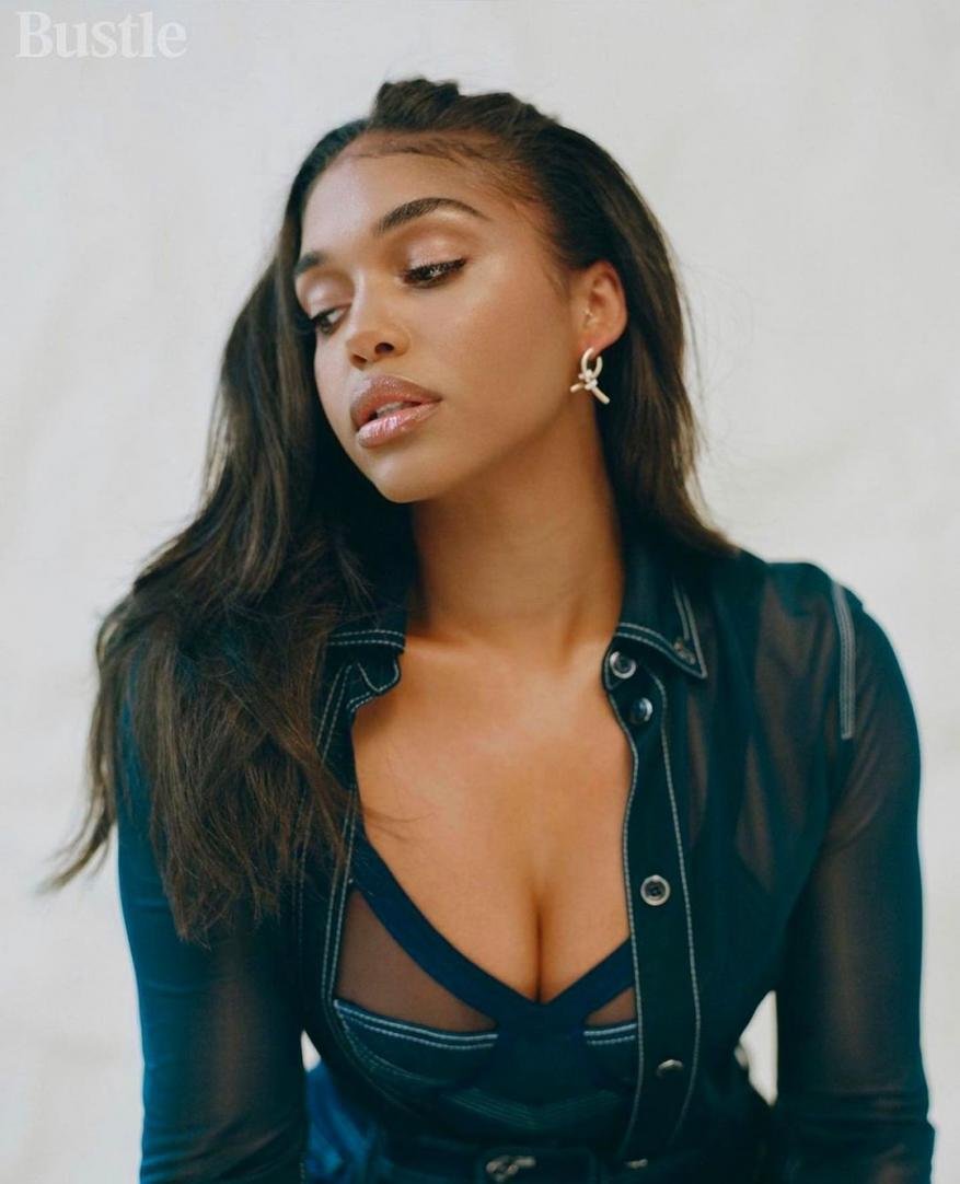 Portrait of a woman with long dark hair wearing a sheer black top with a blue bra underneath, shot in a bright studio setting.