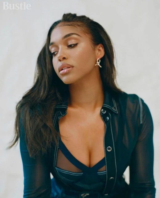 Portrait of a woman with long dark hair wearing a sheer black top with a blue bra underneath, shot in a bright studio setting.