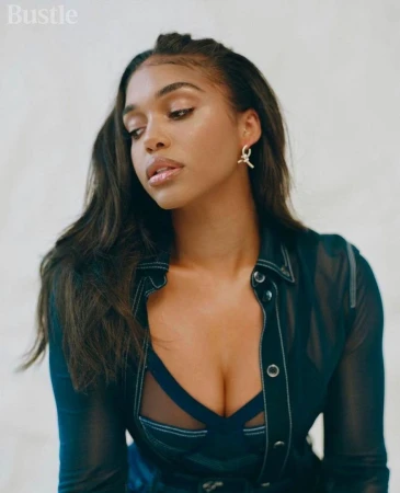 Portrait of a woman with long dark hair wearing a sheer black top with a blue bra underneath, shot in a bright studio setting.
