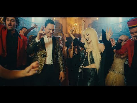 Group of people dancing at a party in a large hall with ornate details and gilded elements, creating a lively and celebratory atmosphere.