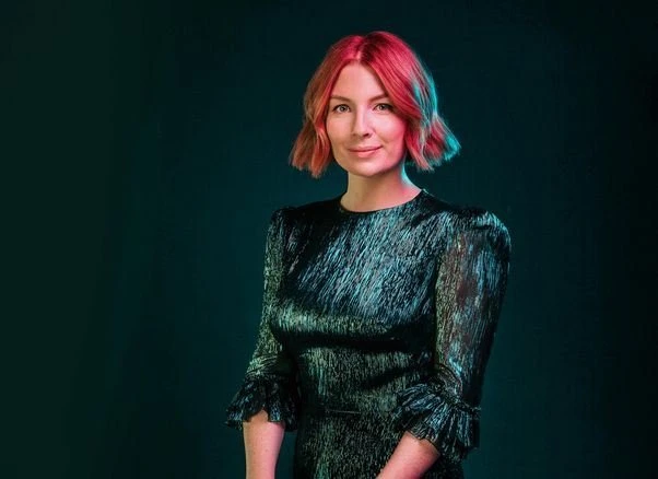 Portrait of a woman with vibrant pink hair wearing a metallic green dress with a dark green background. Beauty and fashion shot.