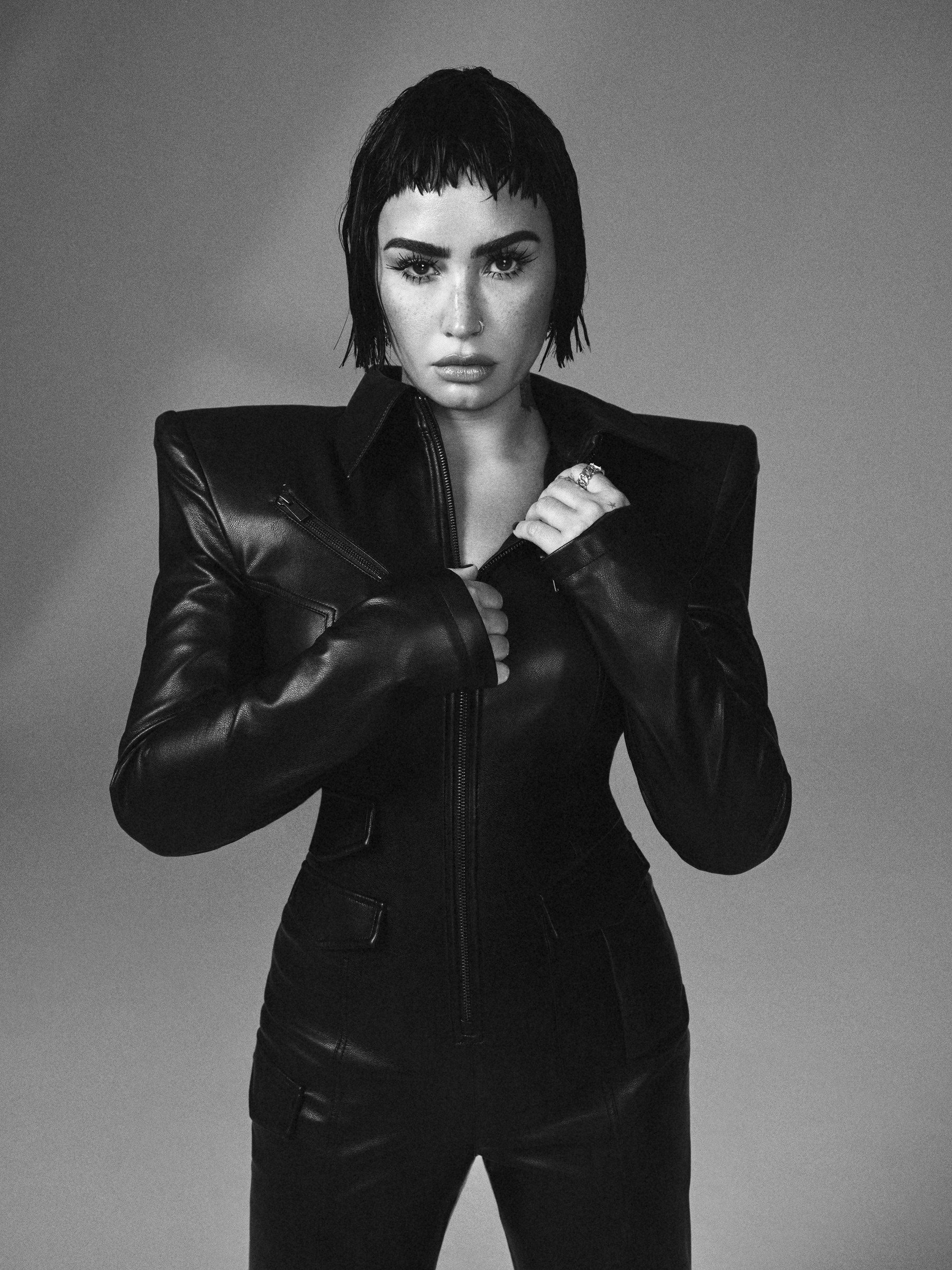 Black and white portrait of an adult female with short dark hair wearing a black jumpsuit. The photo is set against a grey background.