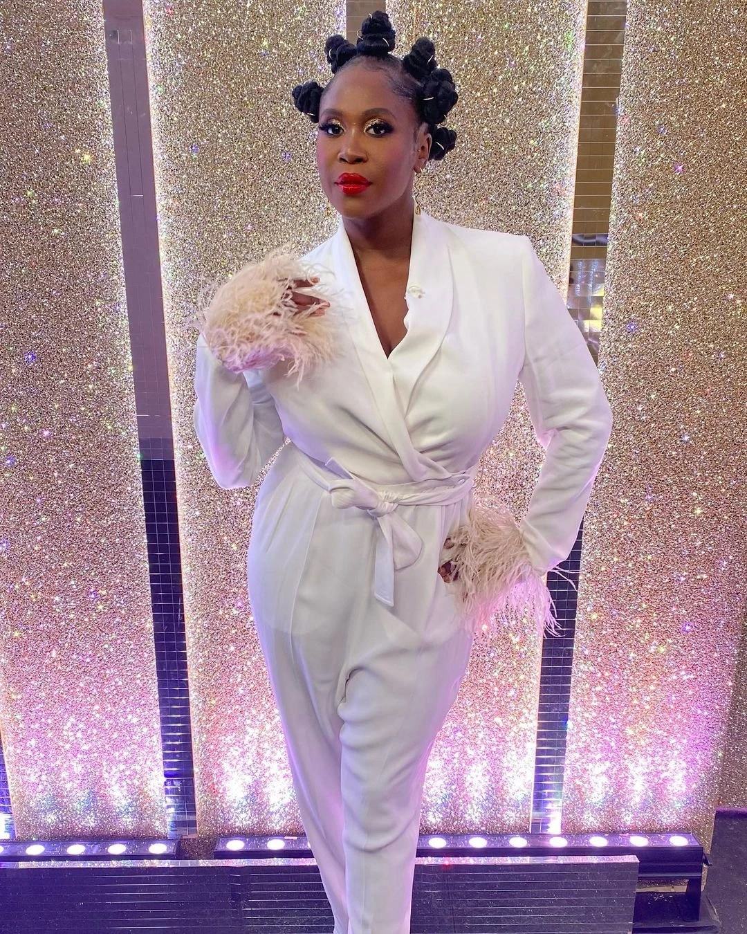 Black woman wearing a white jumpsuit with feathered cuffs and Bantu knots styled by Sinead Mckeefry