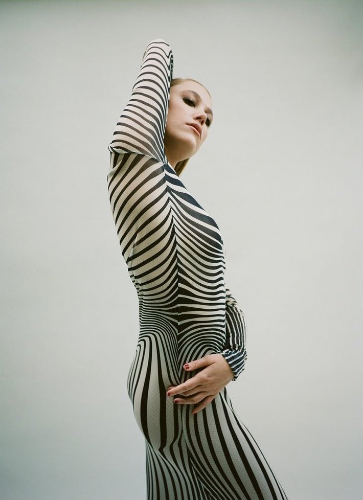 A woman in a black-and-white striped dress poses against a neutral background, showcasing a unique, patterned fashion aesthetic.