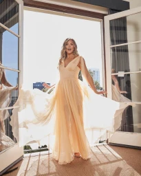 Woman in a flowing pale yellow dress standing in an open doorway with sheer fabric billowing in the sunlight