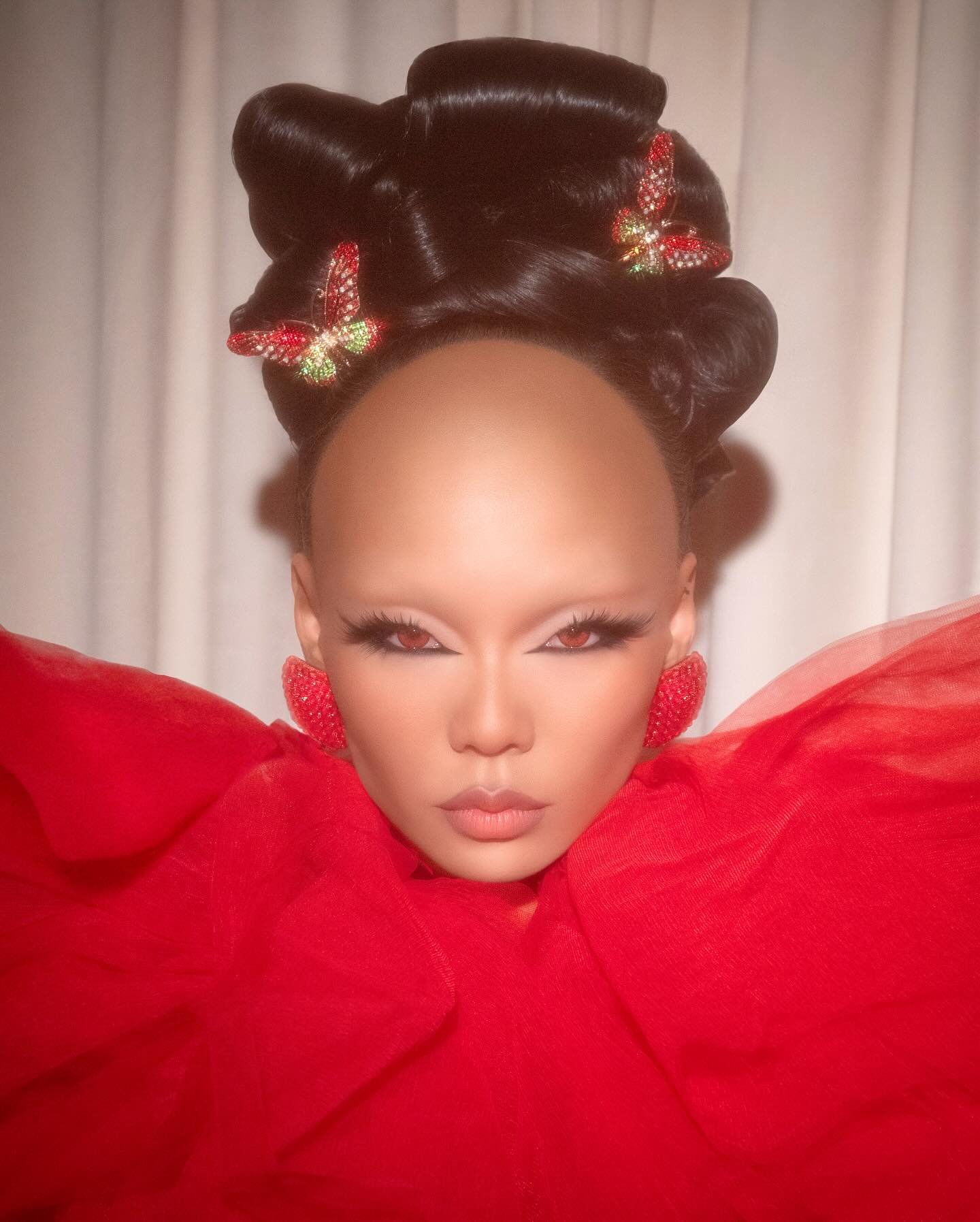 Close-up of a person in red tulle with butterfly hair clips. The person is looking forward and wearing heart-shaped earrings.