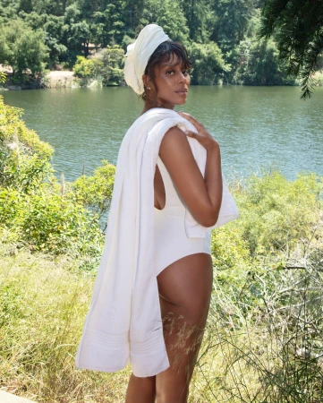 Woman in white swimsuit and head towel holding white towel by a lakeside outdoors in Los Angeles by Steven Simione.