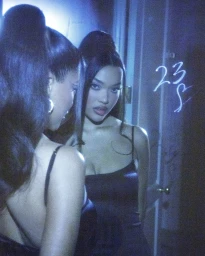 A woman with dark hair in a high ponytail wearing a black dress reflected in a mirror under blue lighting by Steven Simione