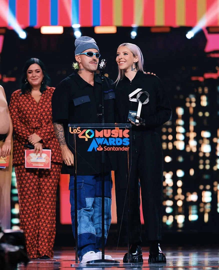 Two music artists on stage accepting an award at 'Los 40 Music Awards' with audience and award sponsor Santander visible.
