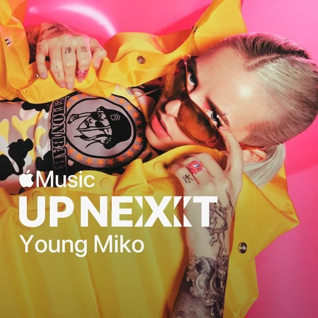 Young Miko is featured on the 'Up Next' Apple Music promotional cover, wearing a yellow jacket and sunglasses against a pink backdrop.