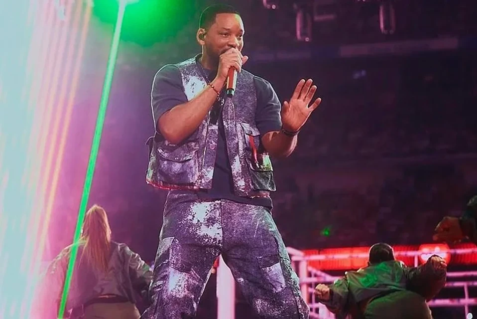 Will Smith performing on stage with dancers, holding microphone. Stage lighting and dancers are in the background.