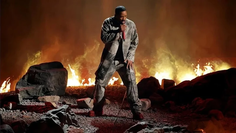 Will Smith singing into a microphone on a rocky ground stage with flames and fire in the background