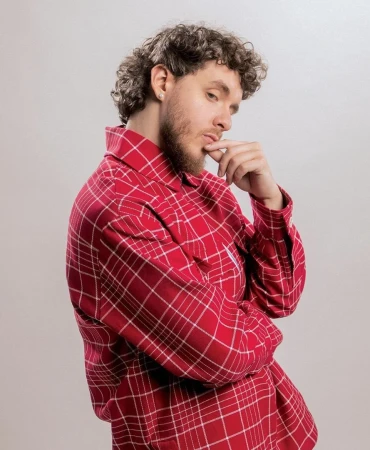Portrait of man with curly brown hair wearing a red plaid shirt against a light grey studio background.