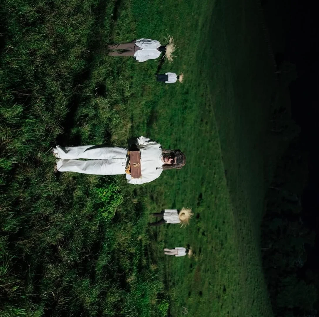 Aerial view of people lying in a grassy field, evoking an otherworldly or dreamlike atmosphere, shot from a high angle.
