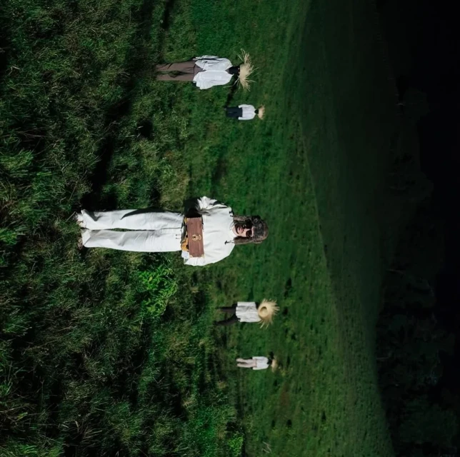 Aerial view of people lying in a grassy field, evoking an otherworldly or dreamlike atmosphere, shot from a high angle.