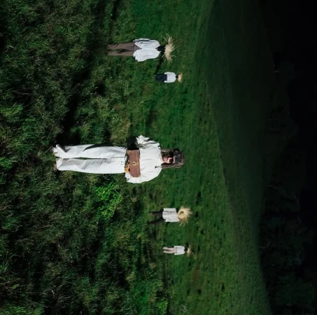 Aerial view of people lying in a grassy field, evoking an otherworldly or dreamlike atmosphere, shot from a high angle.