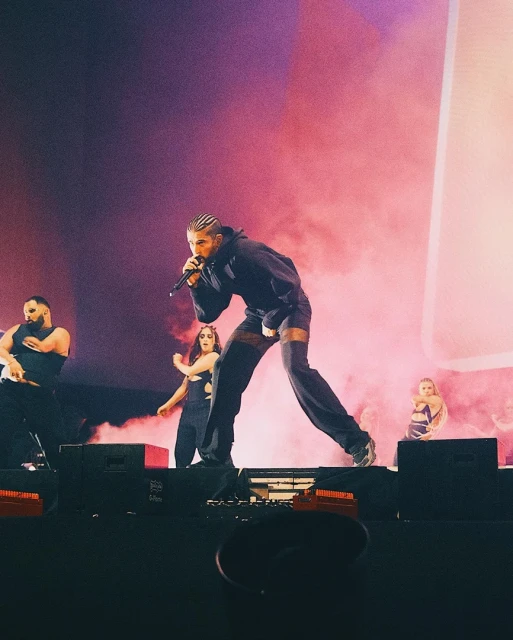 Male singer performs on stage with backup dancers in front of a pink-lit backdrop and a stage filled with theatrical fog.