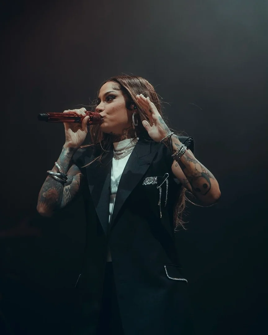 Singer Kehlani performs on stage wearing a black blazer and white shirt. Stage lighting creates dramatic effect for the musician.