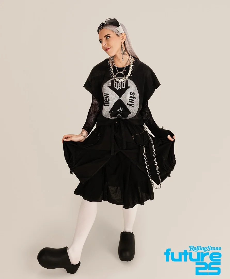 Adult female poses in black alternative fashion dress, platform shoes, and silver hair against a neutral background in a studio shot.