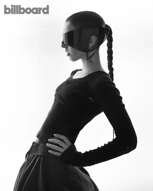 Striking black and white portrait of a young woman with a braided ponytail, wearing futuristic eyewear, against a bright background.