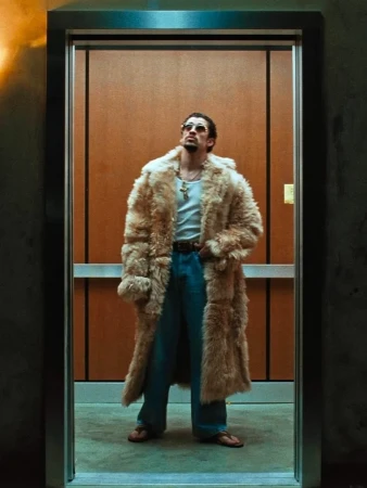 Man wearing a long fluffy fur coat, white tank top, and blue jeans standing inside an elevator