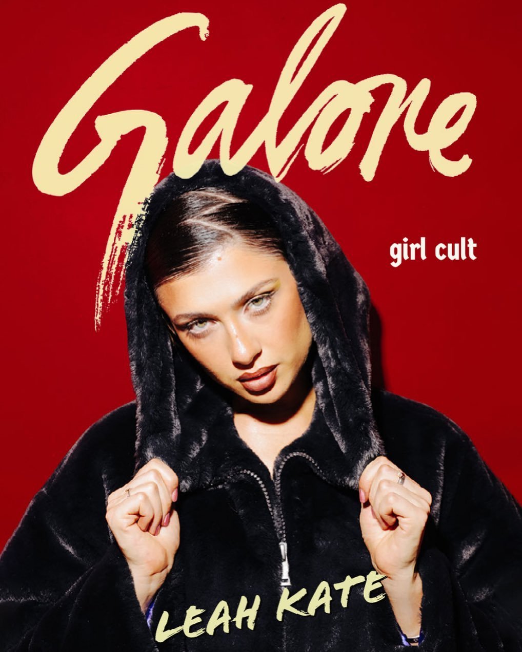 Close-up of a woman with dark hair and green eyes wearing a fur-lined hooded jacket against a red backdrop with stylized text overlays.