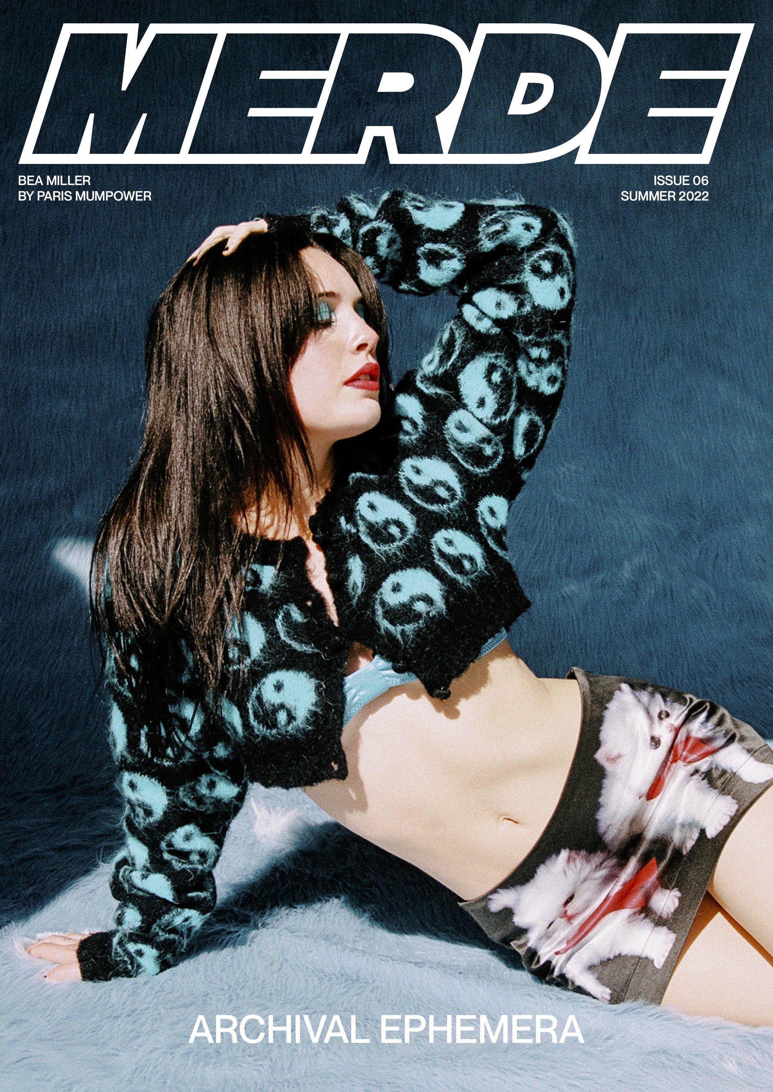 Magazine cover features a brunette model in a patterned cardigan, skirt, and blue lingerie against a textured blue background.