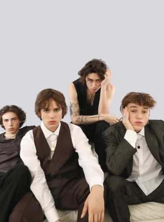 Group portrait of four young adult men in formal wear, posing indoors in a photo studio with a neutral grey background.
