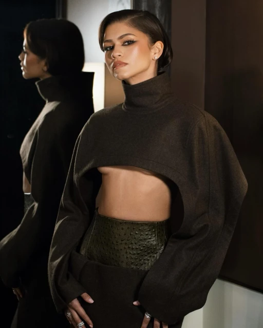 Zendaya poses in studio lighting, showcasing a modern crop top and skirt combination, with a reflected image emphasizing depth.