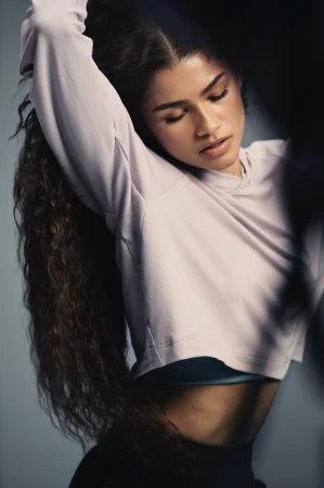 Portrait of a woman with long curly hair wearing a lavender hoodie with a neutral background, showcasing fitness or beauty.