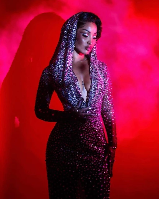 Woman in a sequined dress with a hood poses in a red studio setting with dramatic lighting, showcasing a glamorous and artistic fashion image.