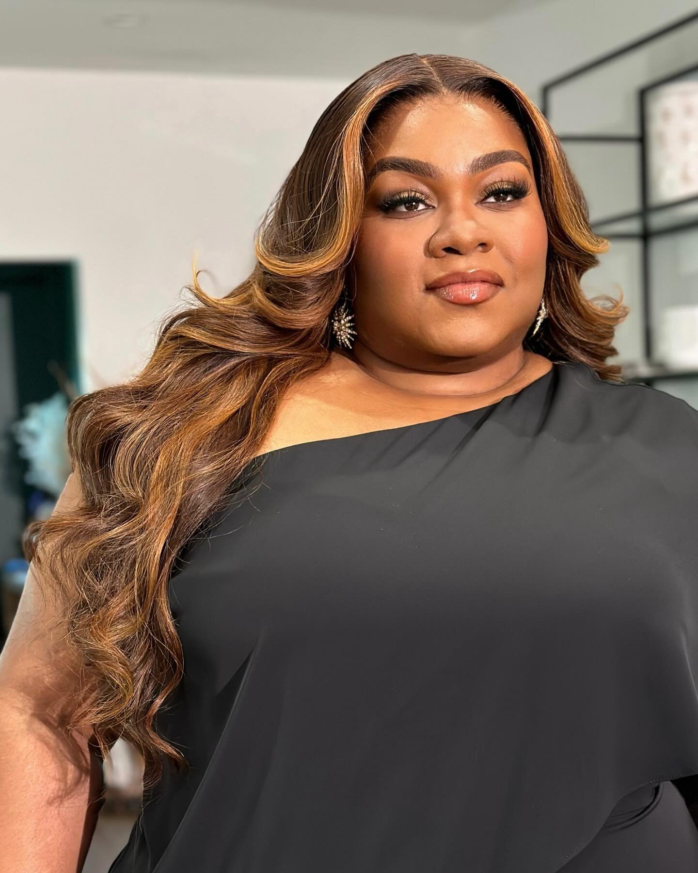 Portrait of a plus-size African-American adult female with long, highlighted hair, wearing a black dress and sparkling earrings.