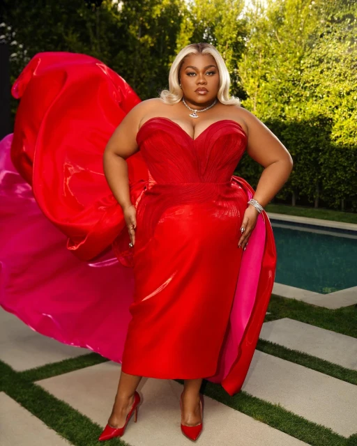 Woman with platinum blonde hair posing in a red strapless gown in front of greenery and a light stone tiled patio.