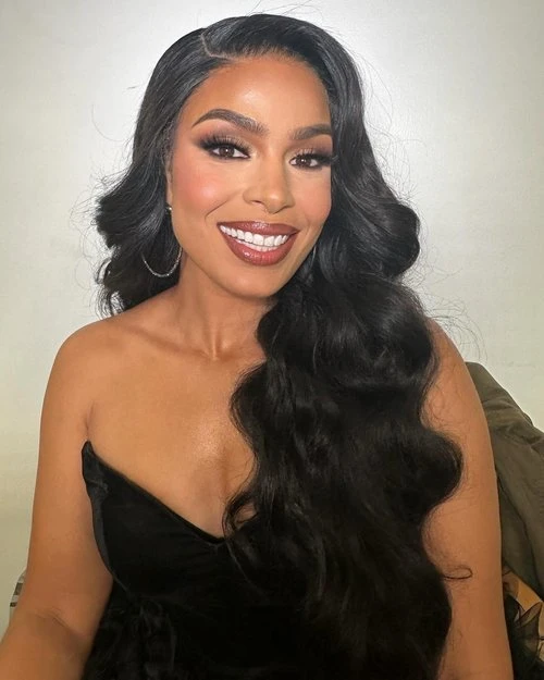Close-up shot of a smiling adult woman with long, wavy black hair, wearing a black strapless top and large hoop earrings.