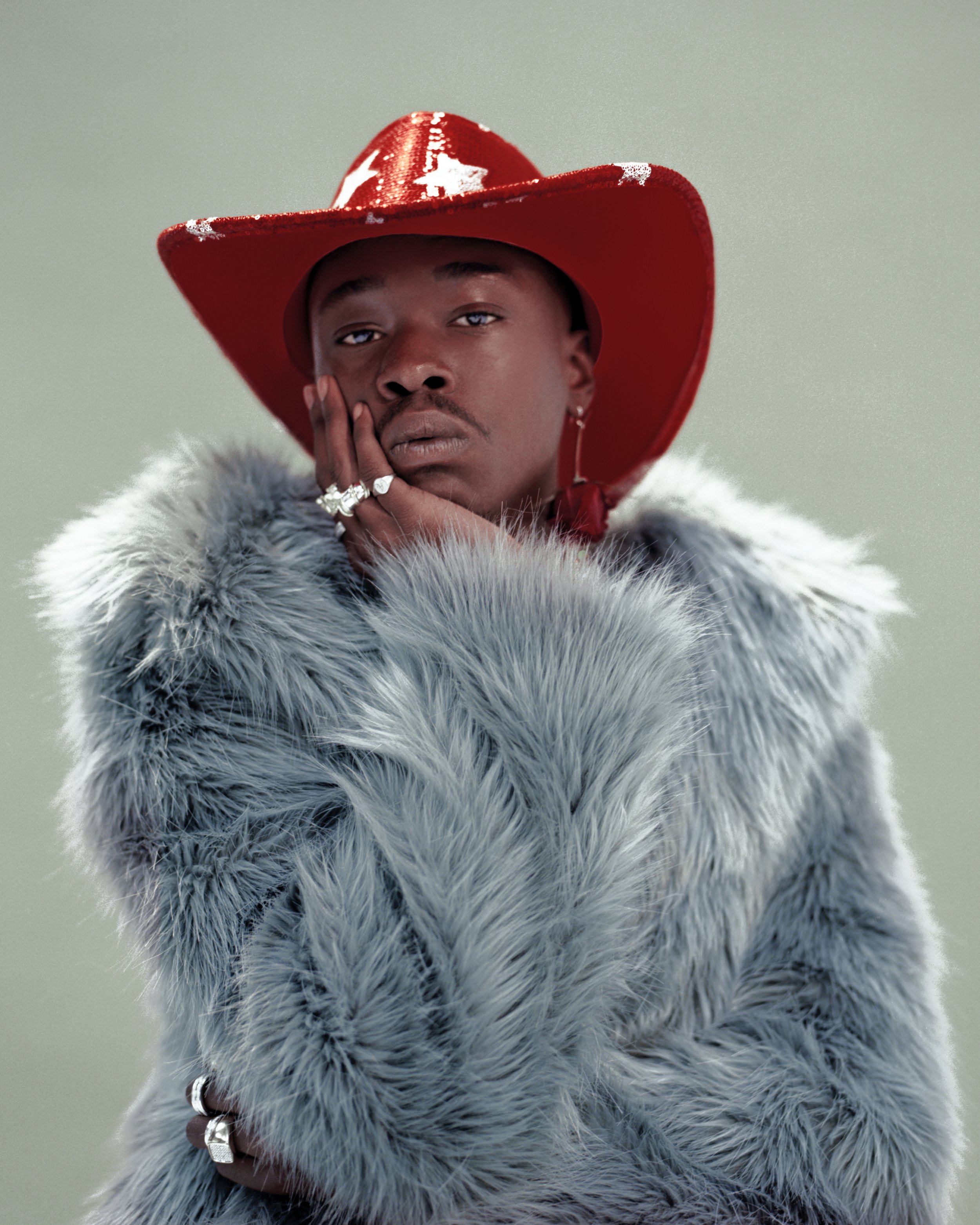 Portrait of Black male model in furry coat and red cowboy hat poses in studio. Stylish editorial shot of fashion and beauty.