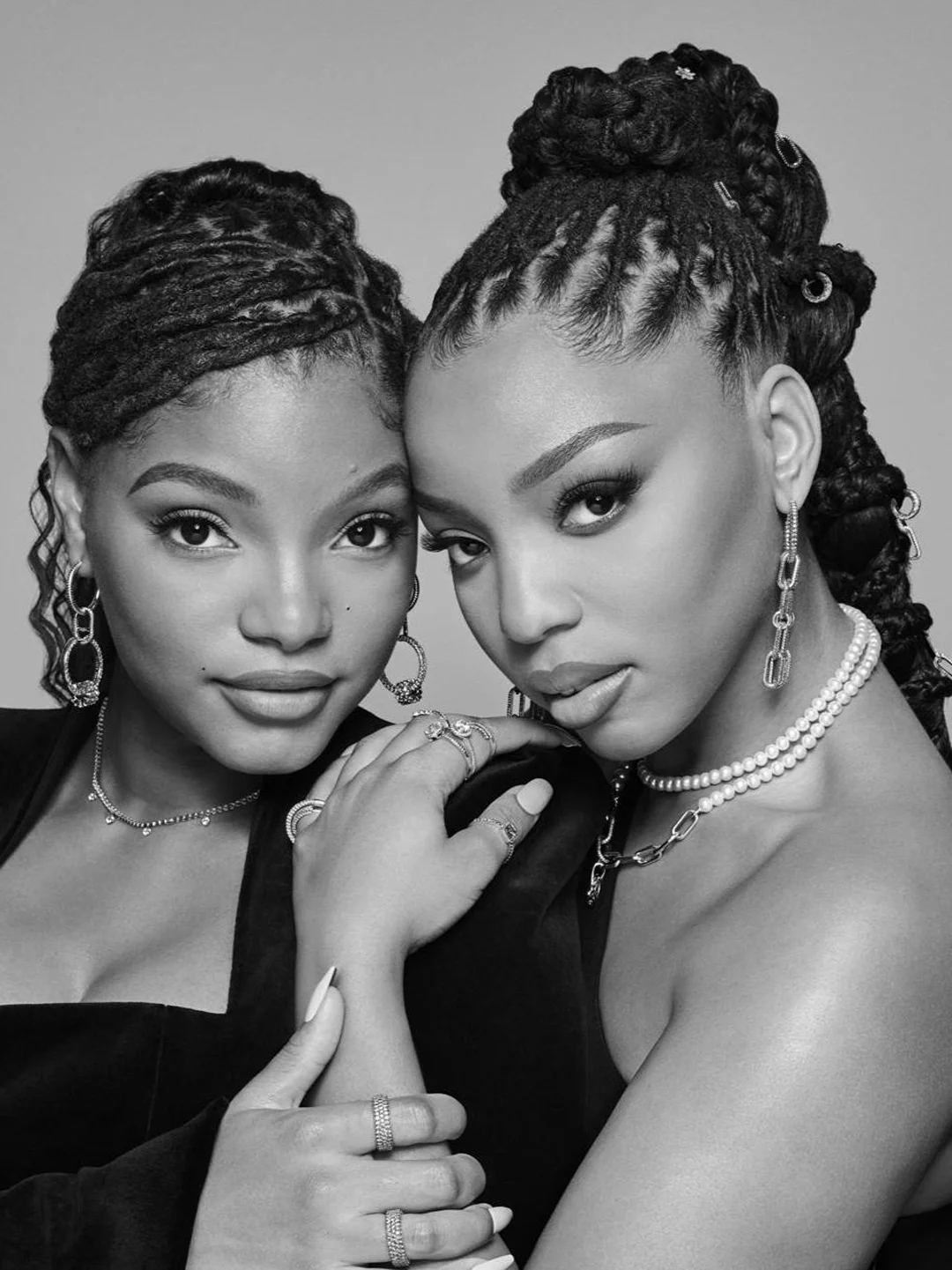Chloe and Halle Bailey posing in a close-up portrait, wearing elegant jewelry, with soft studio lighting and monochromatic colour palette.