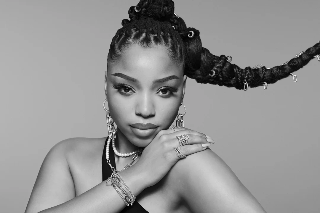 Black and white portrait of a woman with braided hair in a high ponytail, wearing earrings and rings, against a neutral backdrop.
