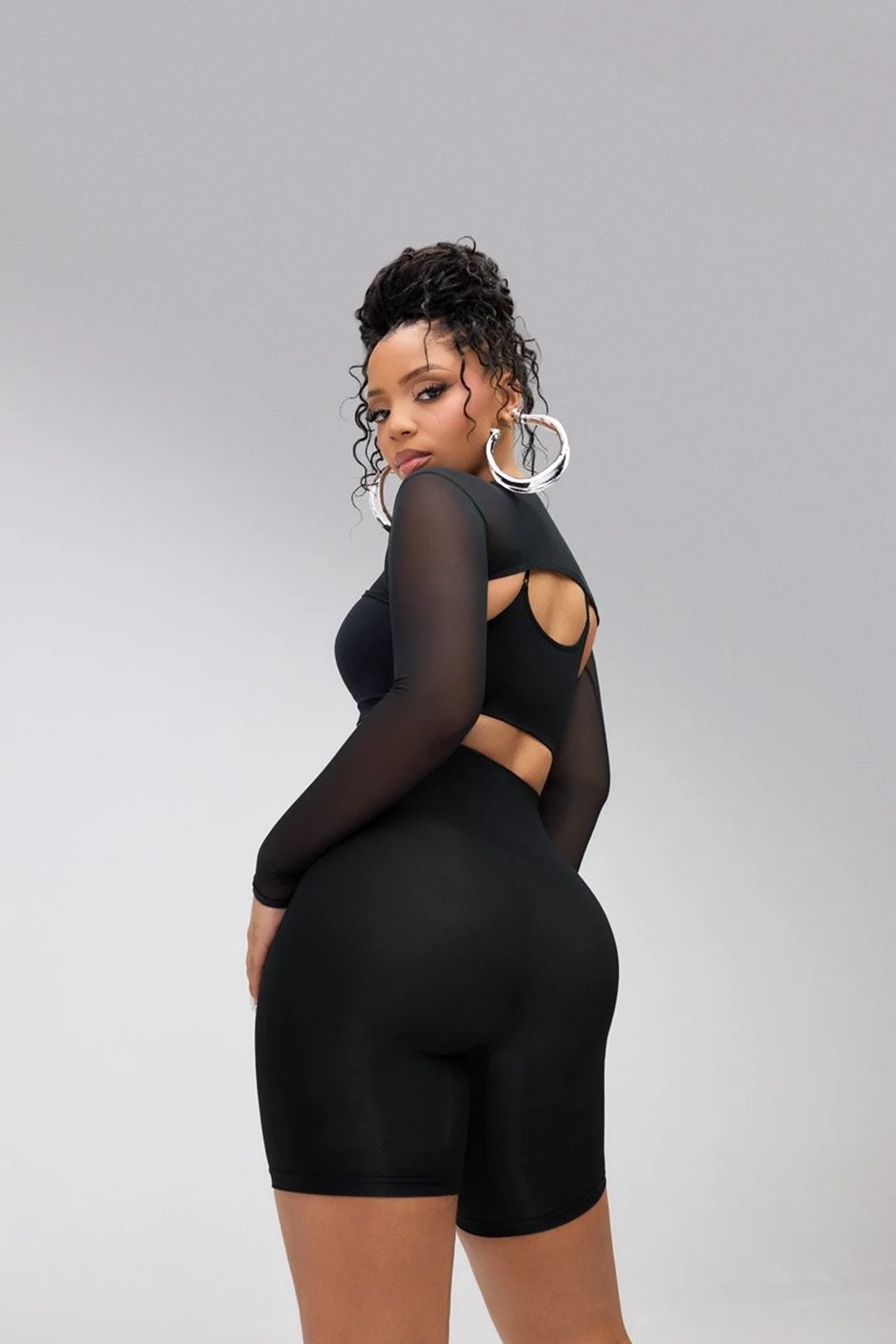 Young adult woman in a black two-piece outfit posing with a slight over-the-shoulder look in a brightly lit photo studio.
