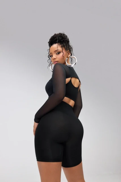Young adult woman in a black two-piece outfit posing with a slight over-the-shoulder look in a brightly lit photo studio.