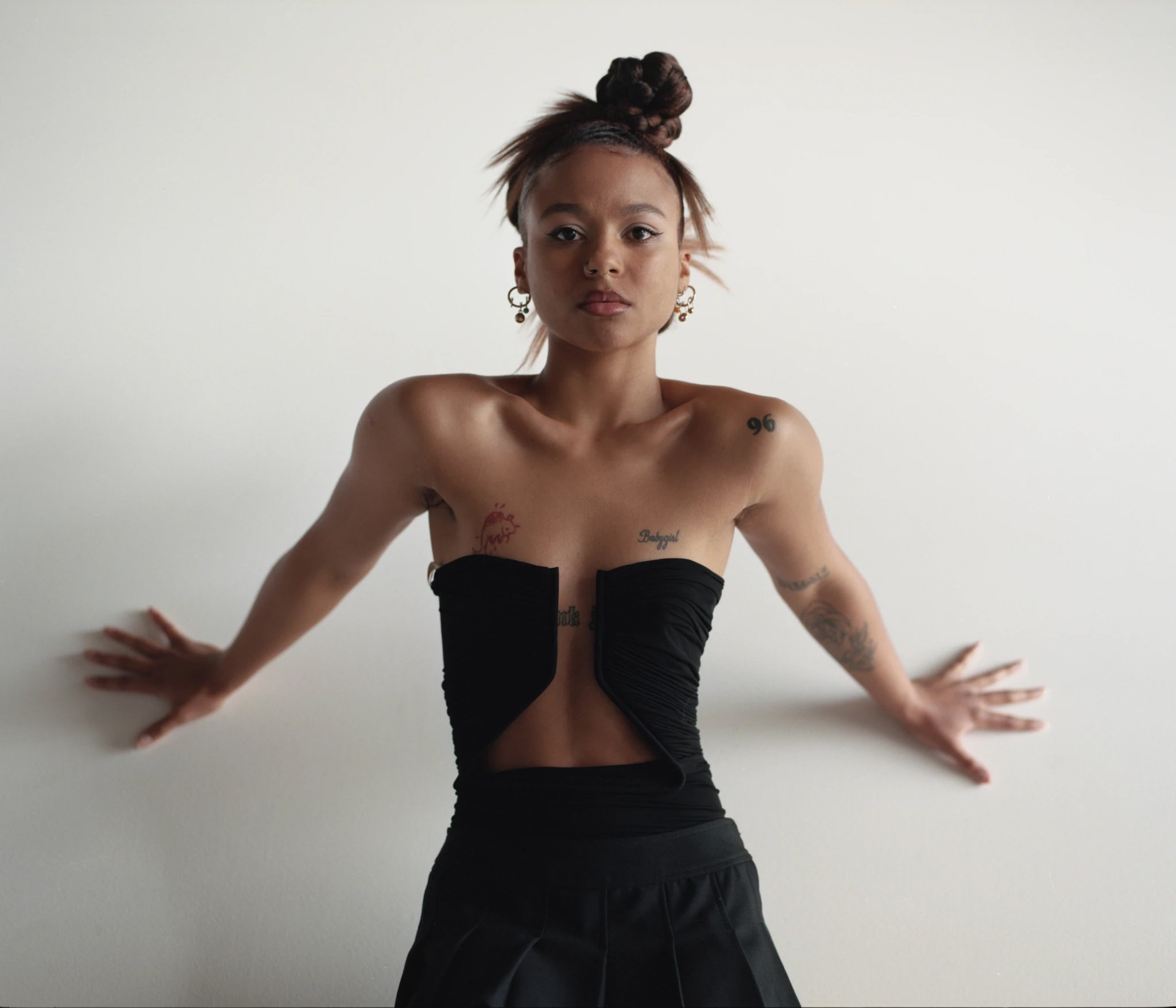 Striking portrait of a young Black woman with an updo, wearing a black top and skirt, posing against a stark white backdrop, showcasing fashion and style.