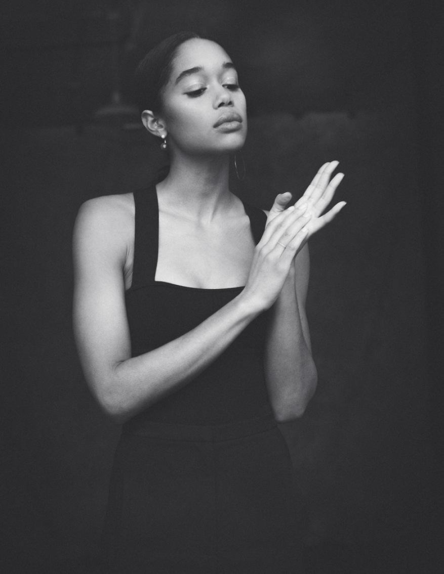 Elegant portrait of an African-American woman in a black dress, striking a pose with hands together, set against a dark background in black and white.