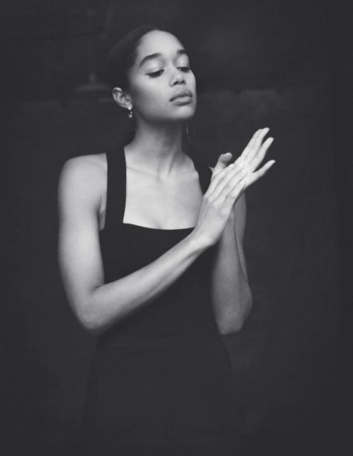 Elegant portrait of an African-American woman in a black dress, striking a pose with hands together, set against a dark background in black and white.