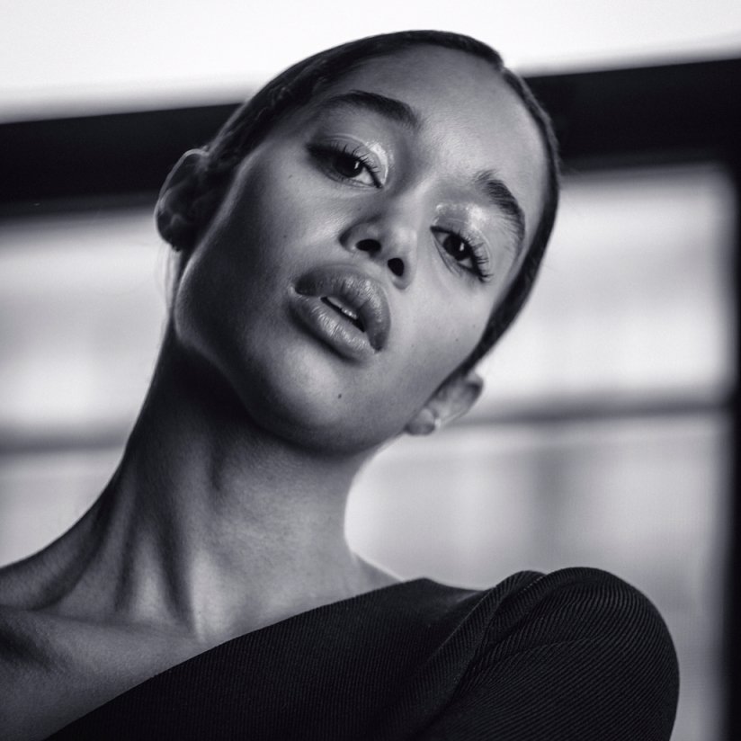Close-up portrait of an African American woman with glossy makeup looking at the camera in a black and white studio setting.