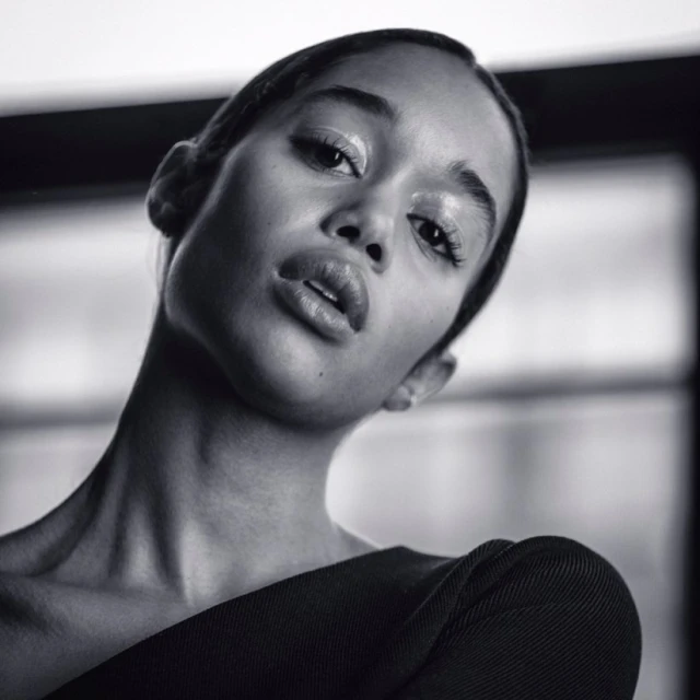 Close-up portrait of an African American woman with glossy makeup looking at the camera in a black and white studio setting.
