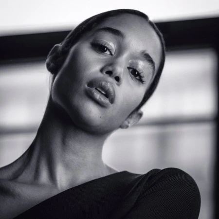 Close-up portrait of an African American woman with glossy makeup looking at the camera in a black and white studio setting.