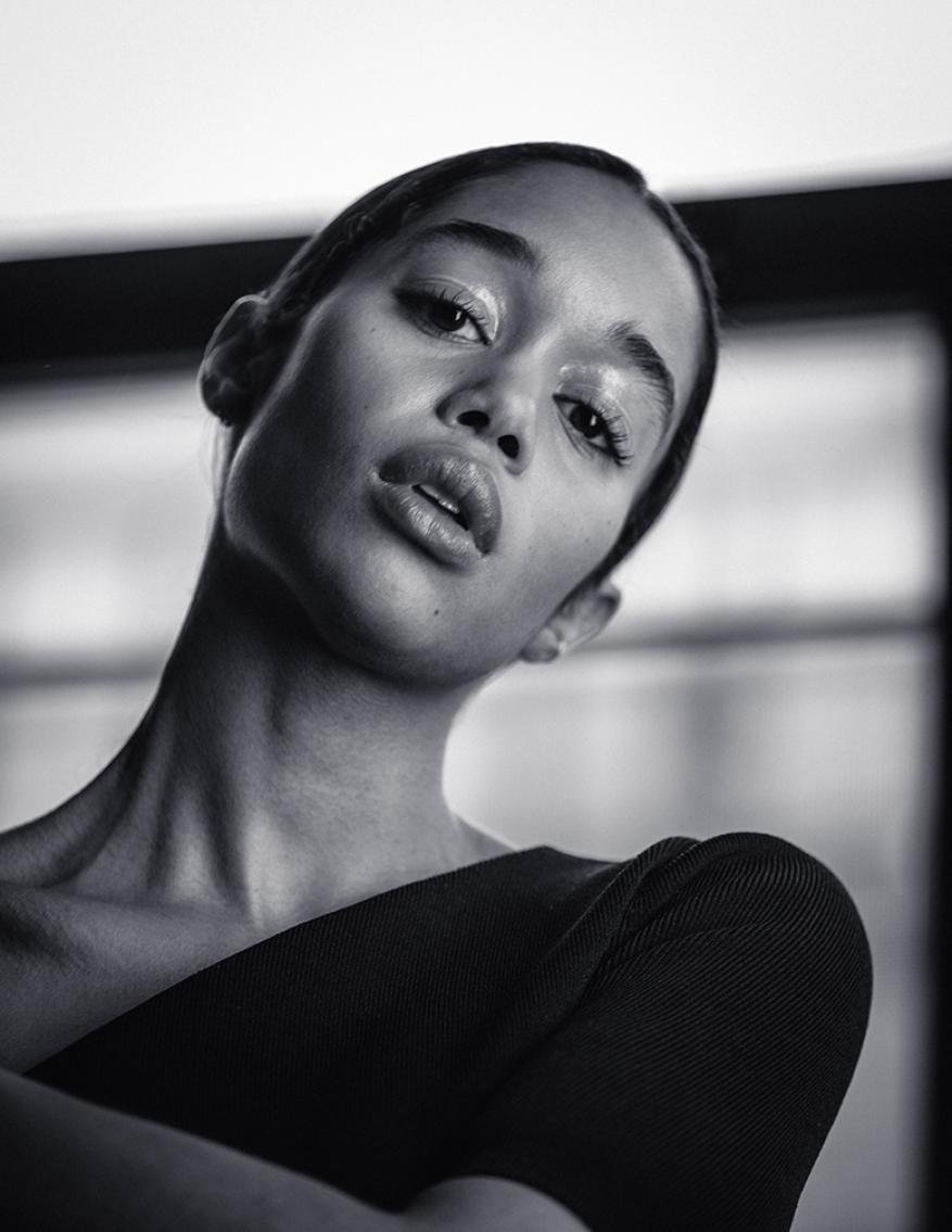Striking black and white portrait of a young woman with glossy makeup, wearing a dark top, captured with a medium shot and eye-level angle.