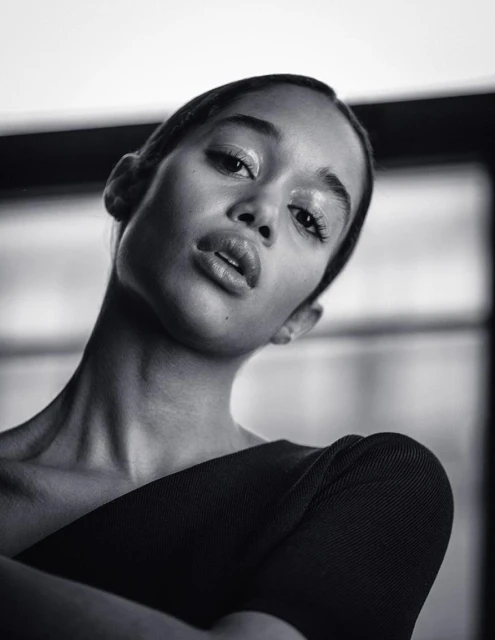 Striking black and white portrait of a young woman with glossy makeup, wearing a dark top, captured with a medium shot and eye-level angle.